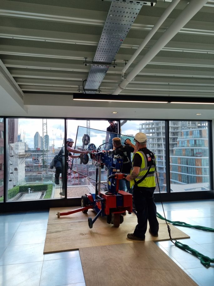 Workers operating machinery near large windows with a city view.