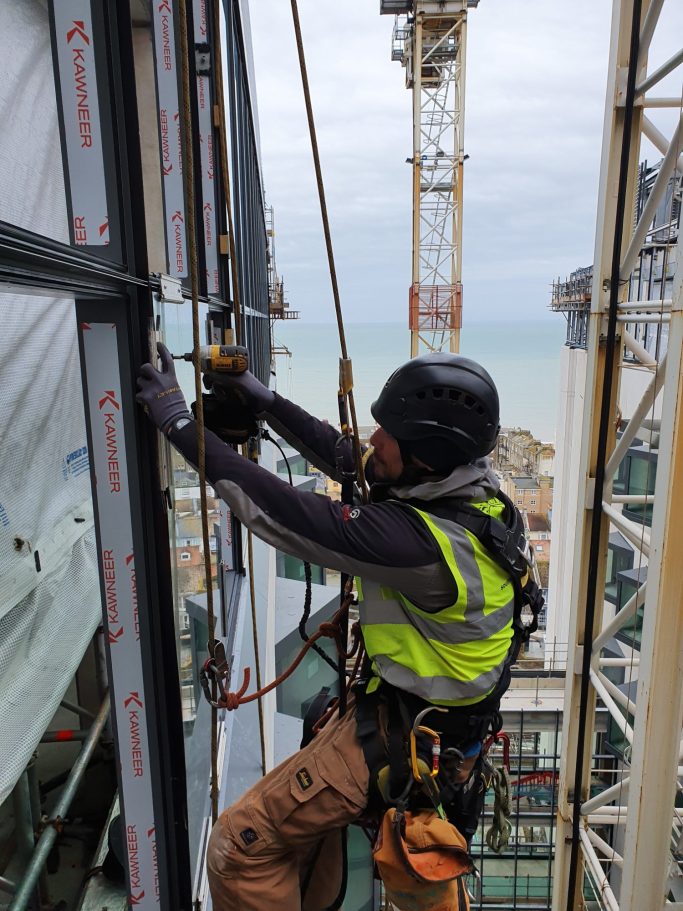 Worker in safety gear operating equipment on a high-rise building site.