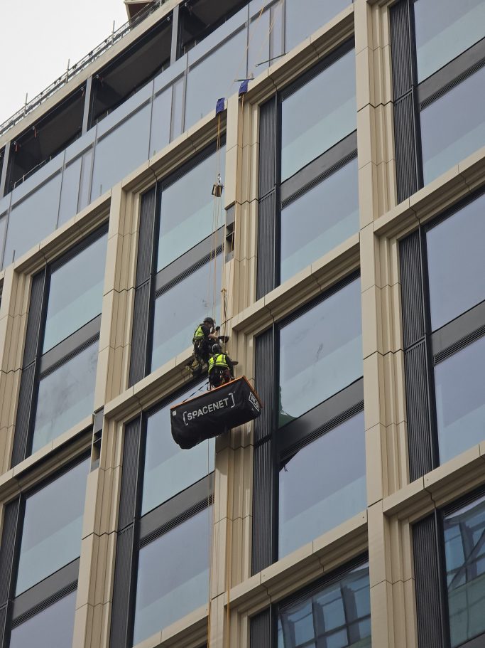 A worker in safety gear using a platform to clean windows on a tall building.